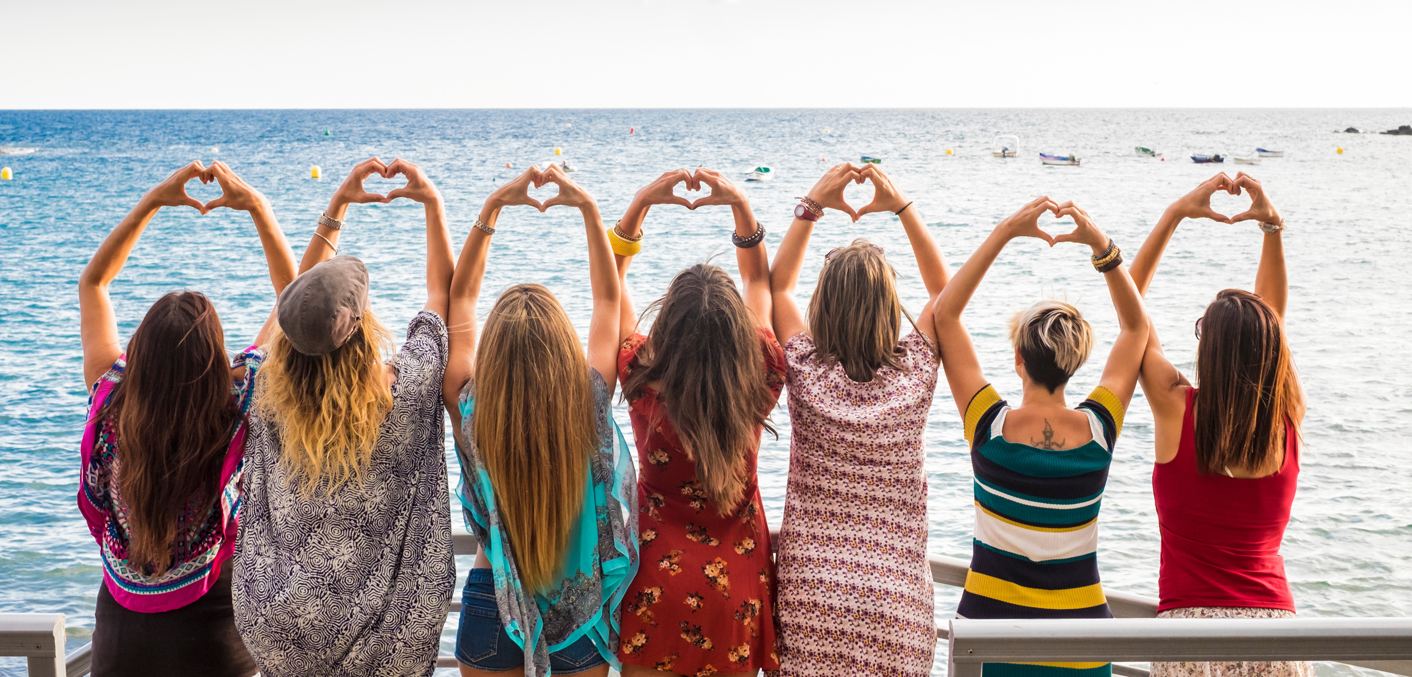 Group of Gen X women forming hearts with their hands by the ocean, symbolizing community, clarity, and connection.